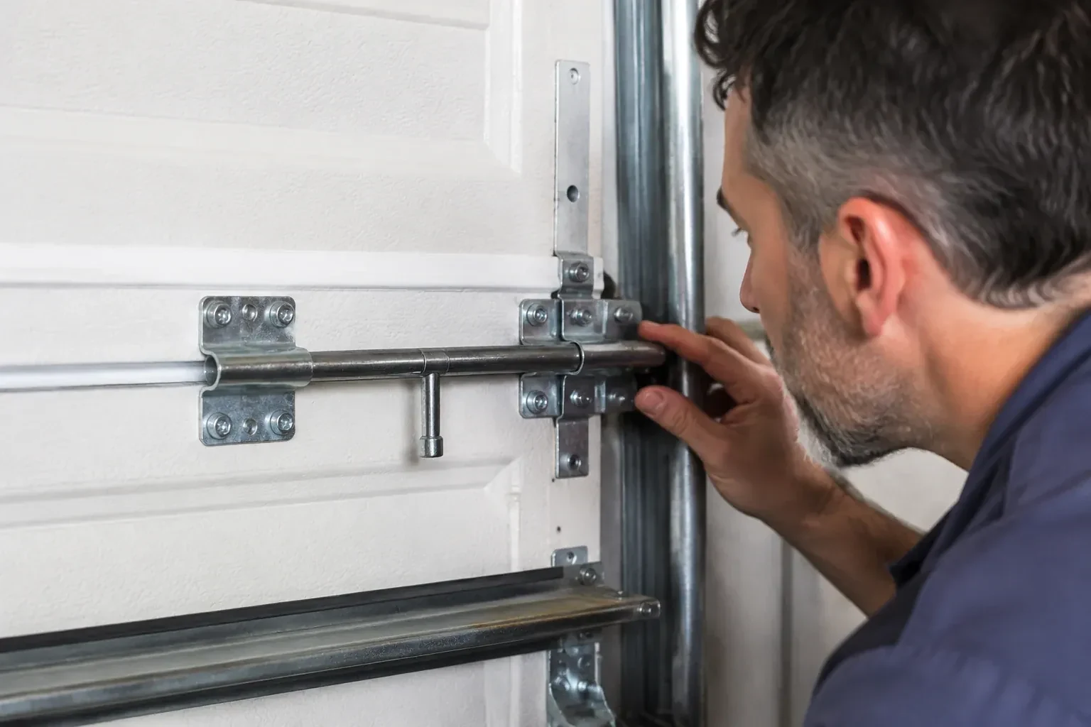 Person leaning close to a white paneled door, one hand on a metal slide-bolt bar mounted across the panel. — Garage Door Manual Lock Repair, Islington